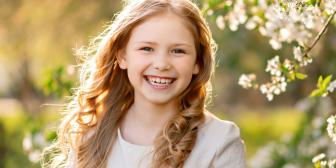 Lächelndes Mädchen im Sonnenlicht zwischen blühenden Bäumen im Frühling.